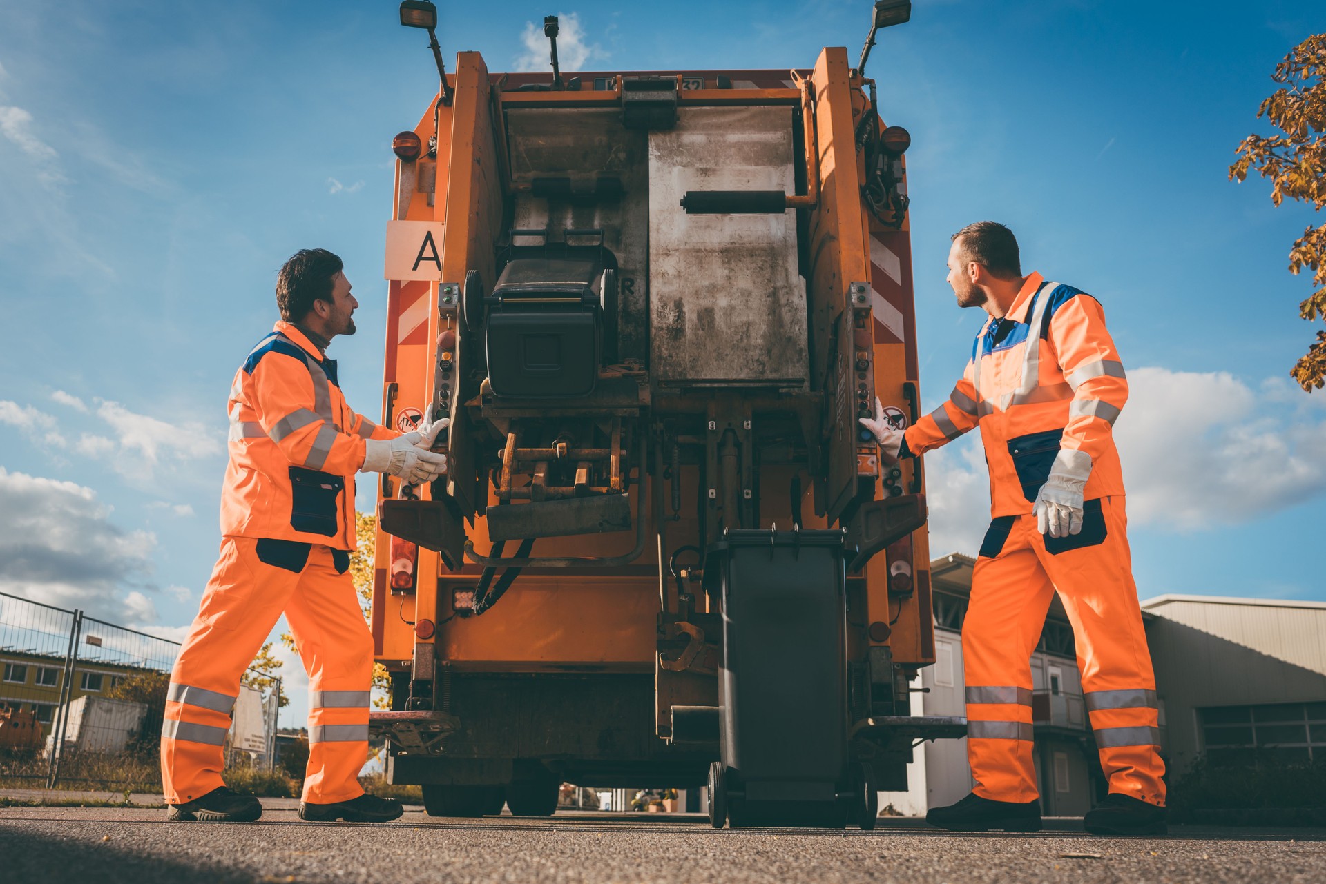 Two refuse collection workers loading garbage into waste truck